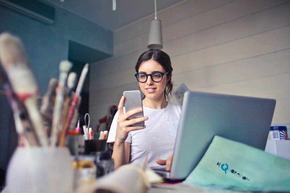 woman on phone near laptop, checking how her home network setup is going