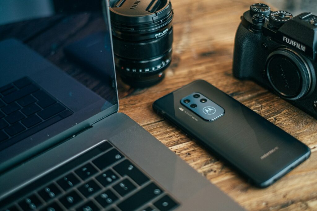 A Motorola phone next to a camera and laptop